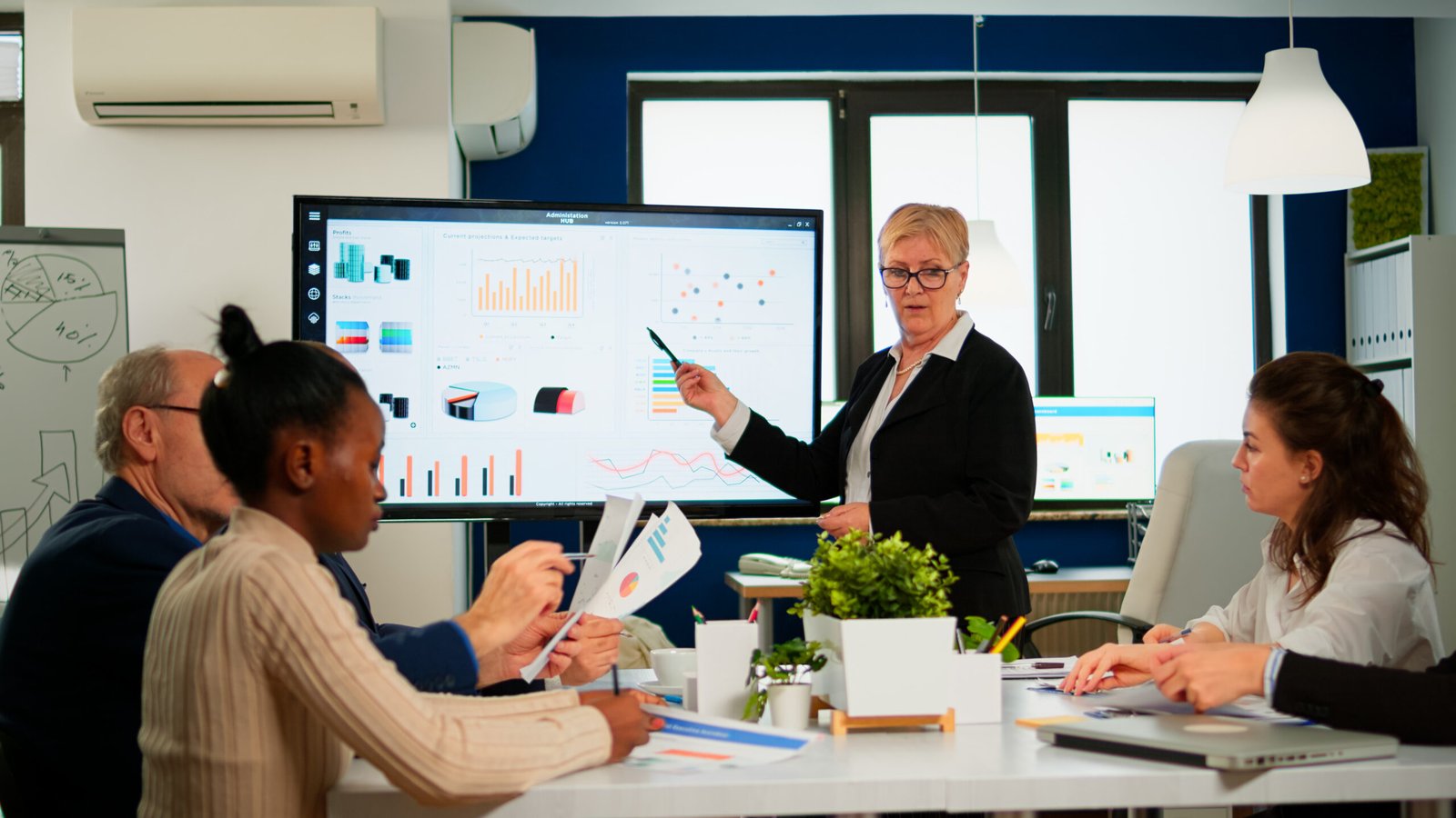 chief analyst holding meeting presentation team economists manager showing digital interactive whiteboard with growth analysis charts statistics data diverse people working broadroom